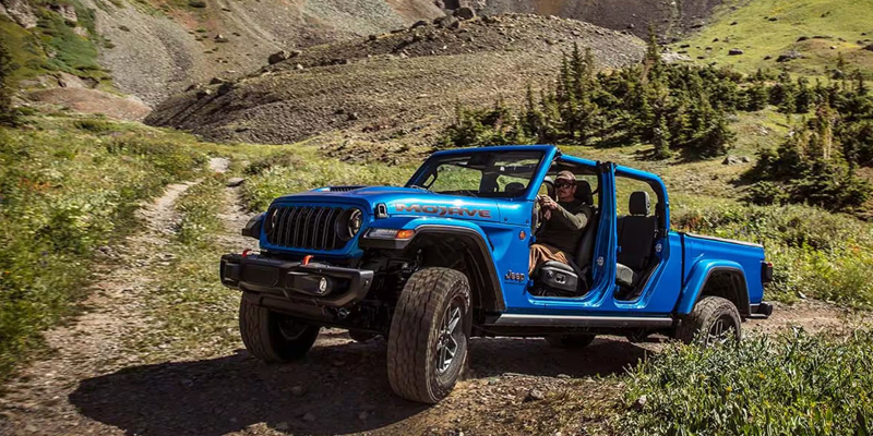 Blue Jeep Gladiator driving on a dirt mountain trail.