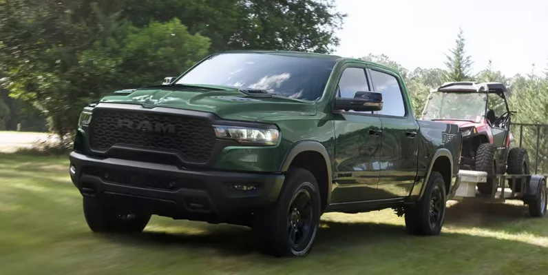A green 2026 RAM 1500 towing a trailer across a grass field.